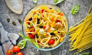 Frischer Spaghetti Salat mit bunten Paprika-, Tomaten- und Olivenstücken, garniert mit Basilikum.