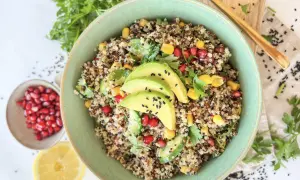 Bunter Quinoa Salat mit Avocado, Granatapfelkernen, Mais und Petersilie, garniert mit schwarzen Sesamkörnchen.