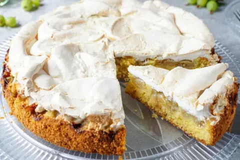 Ein saftiger Stachelbeer Baiser Kuchen mit goldbraunem Boden und fluffiger Baiserhaube, ein Stück ist angeschnitten.