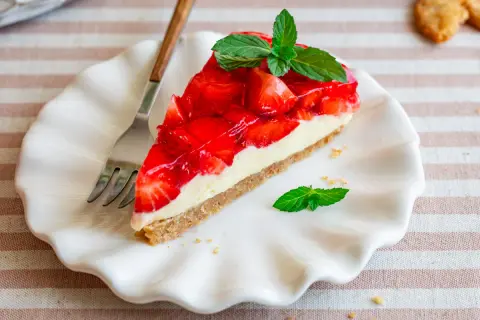 Ein Stück Kuchen ohne Backen mit Keksboden, belegt mit frischen Erdbeeren und Sahne, garniert mit Minze.