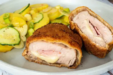 Zwei goldbraune Cordon Bleu, gefüllt mit Schinken und Käse, daneben ein bunter Kartoffel-Zucchini-Salat. Ein leckeres Cordon Bleu Rezept!