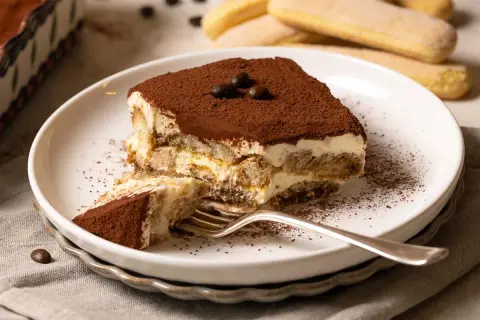 Ein Stück Tiramisu, perfekt für ein Tiramisu Rezept. Mit Löffelbiskuits, Creme und Kakaopulver bestäubt.