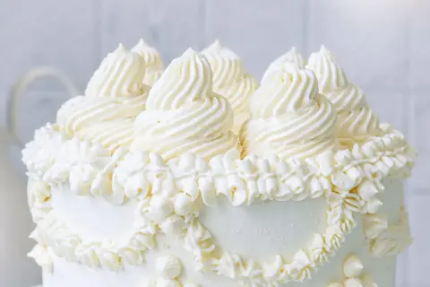 Ein weißer Kuchen, üppig dekoriert mit amerikanischer Buttercreme in kunstvollen Tupfen und Rüschen.