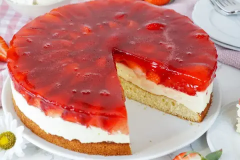 Erdbeerkuchen mit Biskuitboden, Vanillepudding und frischen Erdbeeren unter rotem Tortenguss. Ein saftiges Stück wartet!