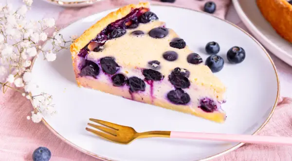 Ein Stück Heidelbeerkuchen Landfrauenart auf einem Teller, garniert mit frischen Heidelbeeren und einer kleinen Gabel.