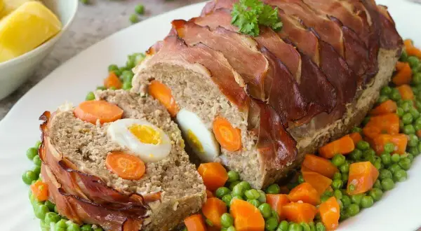 Ein saftiger falscher Hase, umwickelt mit Speck, serviert auf Erbsen und Karotten.