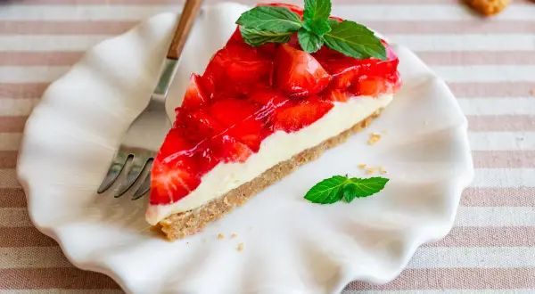 Ein Stück Kuchen ohne Backen mit Keksboden, belegt mit frischen Erdbeeren und Sahne, garniert mit Minze.