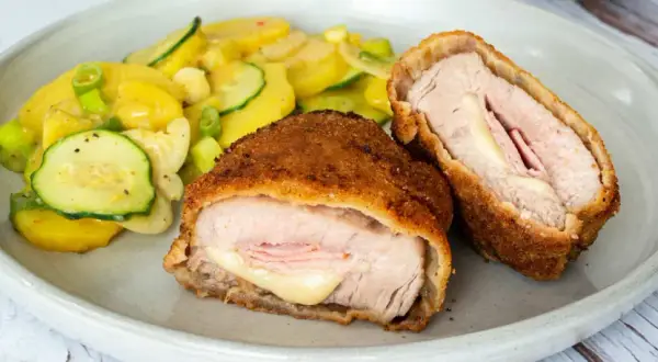 Zwei goldbraune Cordon Bleu, gefüllt mit Schinken und Käse, daneben ein bunter Kartoffel-Zucchini-Salat. Ein leckeres Cordon Bleu Rezept!