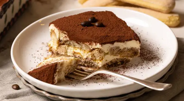 Ein Stück Tiramisu, perfekt für ein Tiramisu Rezept. Mit Löffelbiskuits, Creme und Kakaopulver bestäubt.