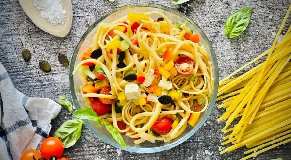 Frischer Spaghetti Salat mit bunten Paprika-, Tomaten- und Olivenstücken, garniert mit Basilikum.