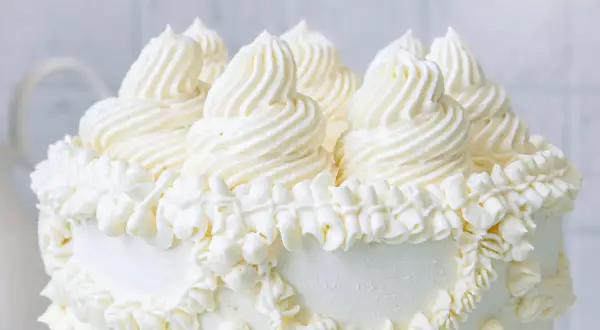 Ein weißer Kuchen, üppig dekoriert mit amerikanischer Buttercreme in kunstvollen Tupfen und Rüschen.