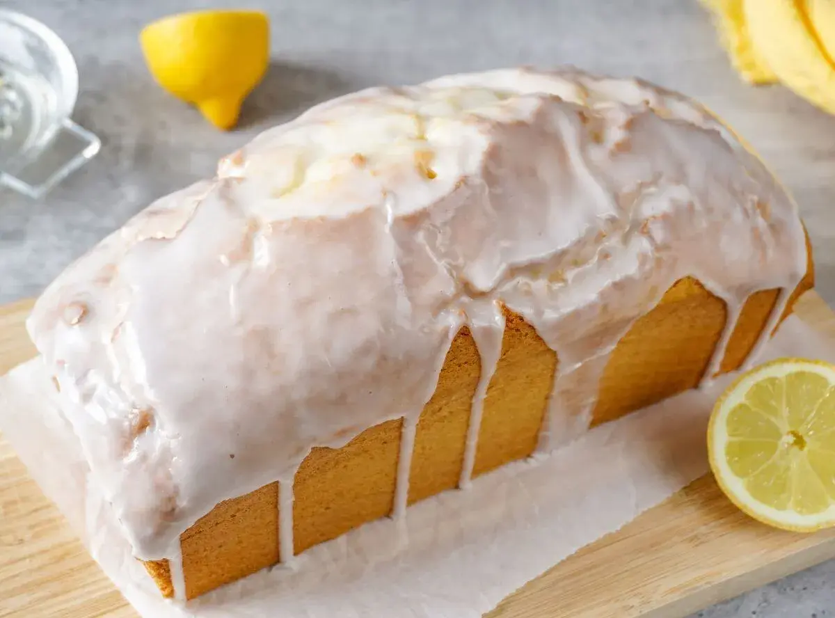 Ein saftiger Zitronenkuchen in Kastenform, überzogen mit süßem Zuckerguss. Ein Zitronenstück liegt daneben.