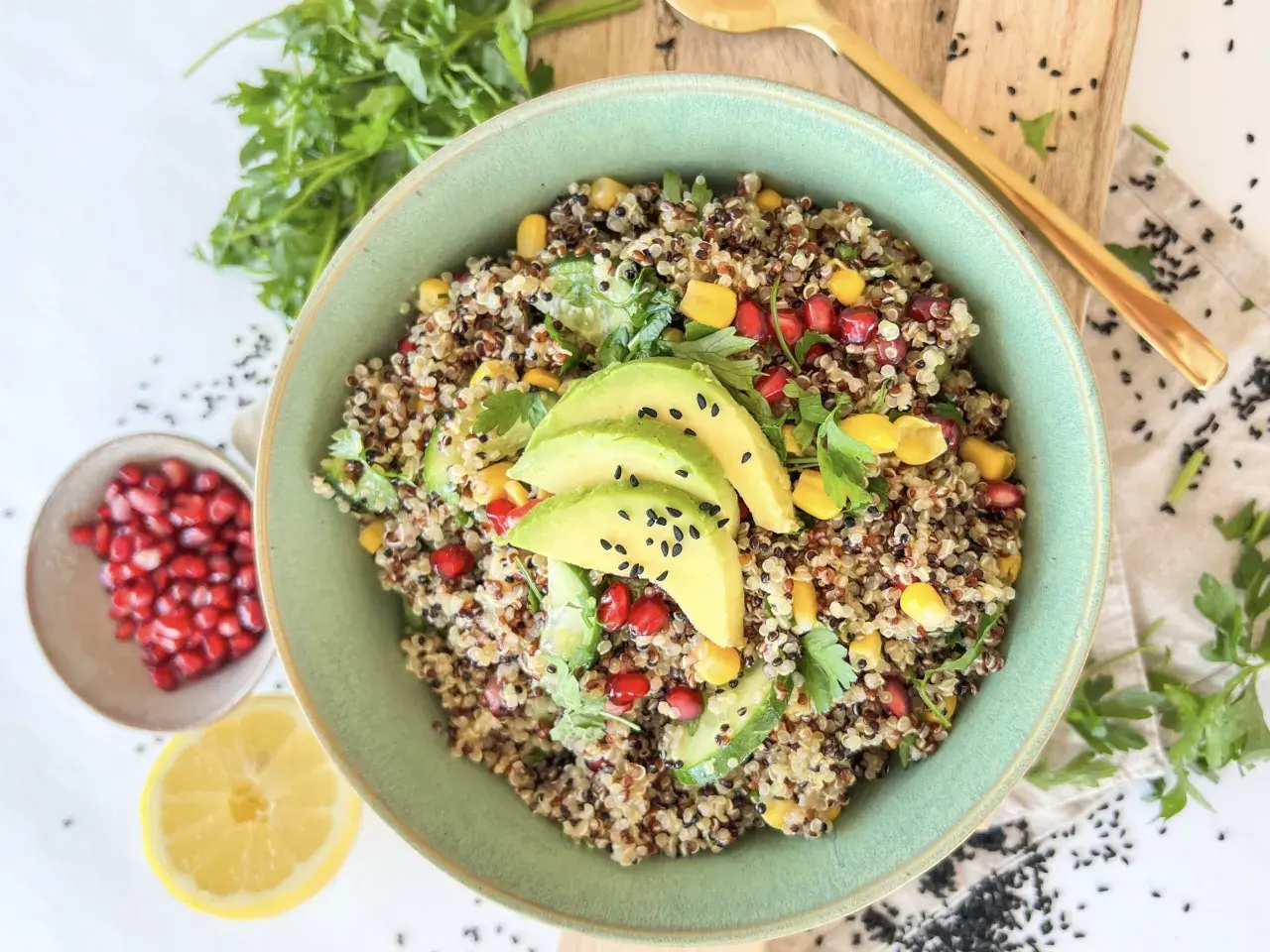 Bunter Quinoa Salat mit Avocado, Granatapfelkernen, Mais und Petersilie, garniert mit schwarzen Sesamkörnchen.