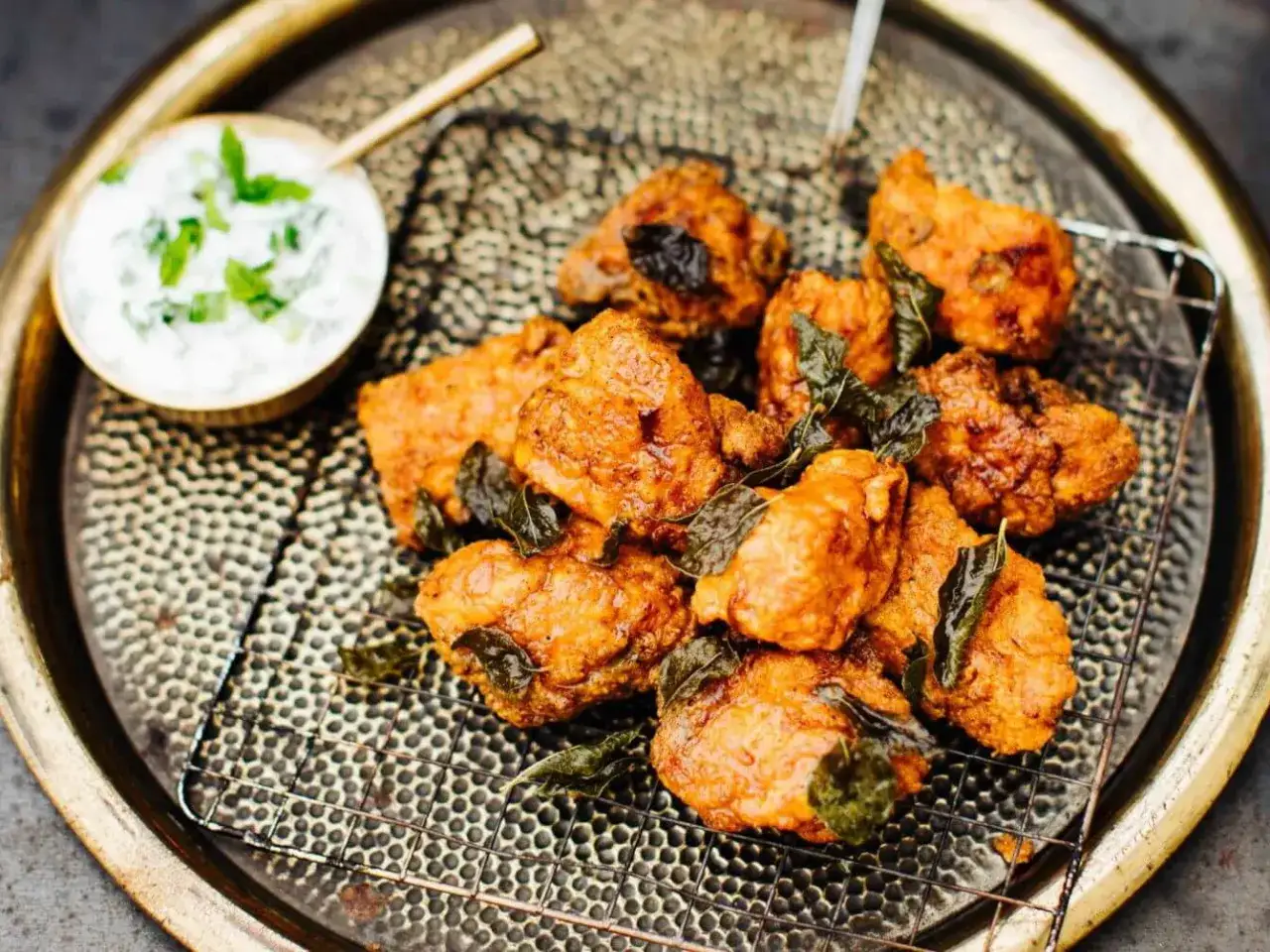 Knusprige chicken pakora mit frischen Kr&auml;utern und einem Dip auf einem dekorativen Tablett.