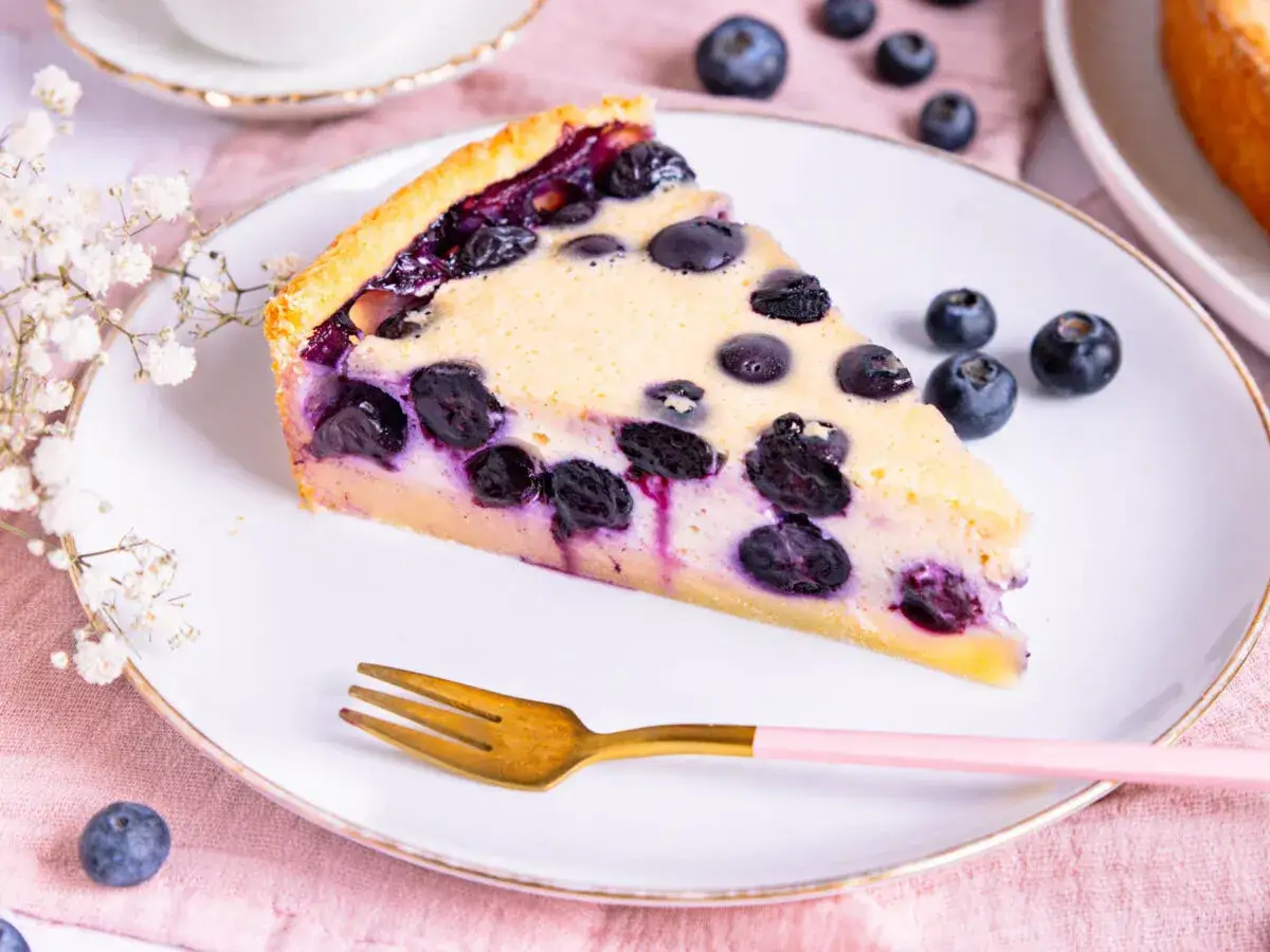 Ein Stück Heidelbeerkuchen Landfrauenart auf einem Teller, garniert mit frischen Beeren und zarten Blüten.
