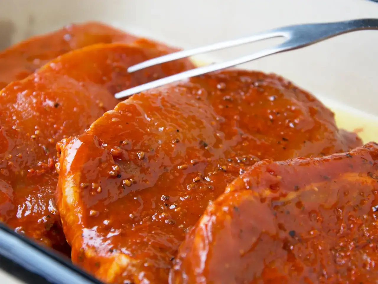Zartes Schweinefleisch marinieren in einer w&uuml;rzigen Sauce. Eine Gabel liegt bereit, um die saftigen St&uuml;cke zu wenden.
