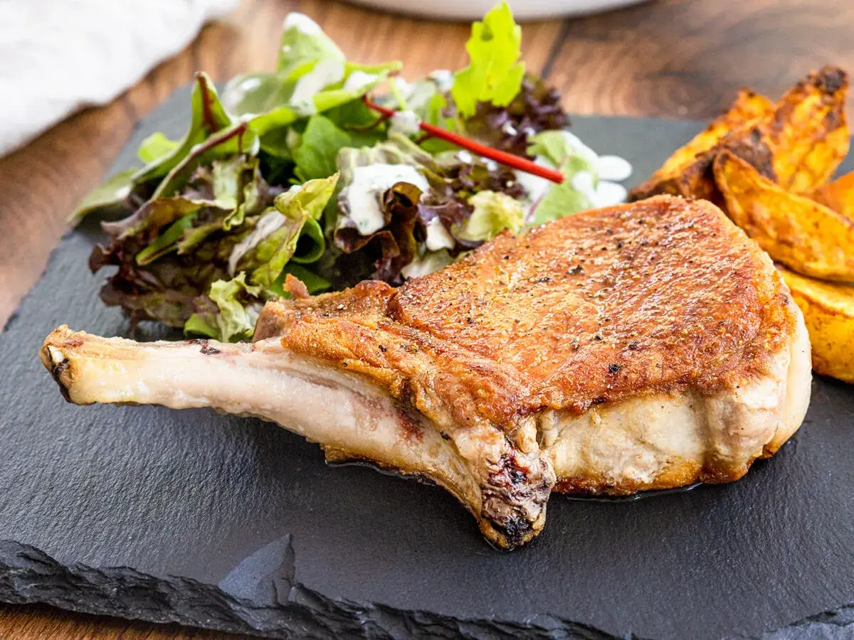 Ein saftiges Kotelett braten, serviert mit knusprigen Kartoffelspalten und frischem Salat.