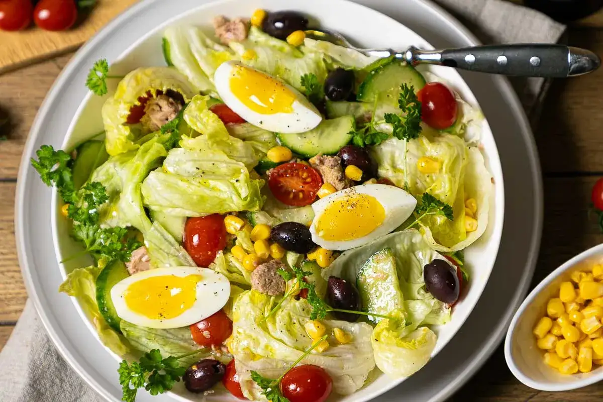 Ein klassischer Thunfischsalat mit knackigem Salat, Tomaten, Gurken, Oliven, Mais und gekochten Eiern.
