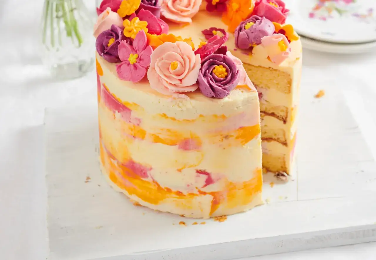 Bunter Kuchen mit amerikanischer Buttercreme-Blumen und Marmorierung. Ein Stück ist herausgeschnitten.