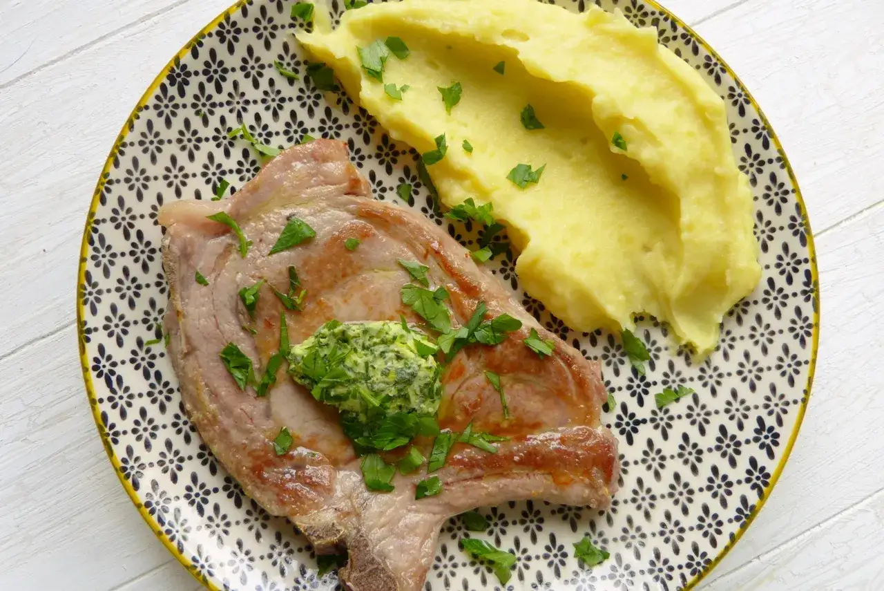 Perfekt gegartes Kalbskotelett sous vide mit Kräuterbutter und cremigem Kartoffelpüree, garniert mit Petersilie.