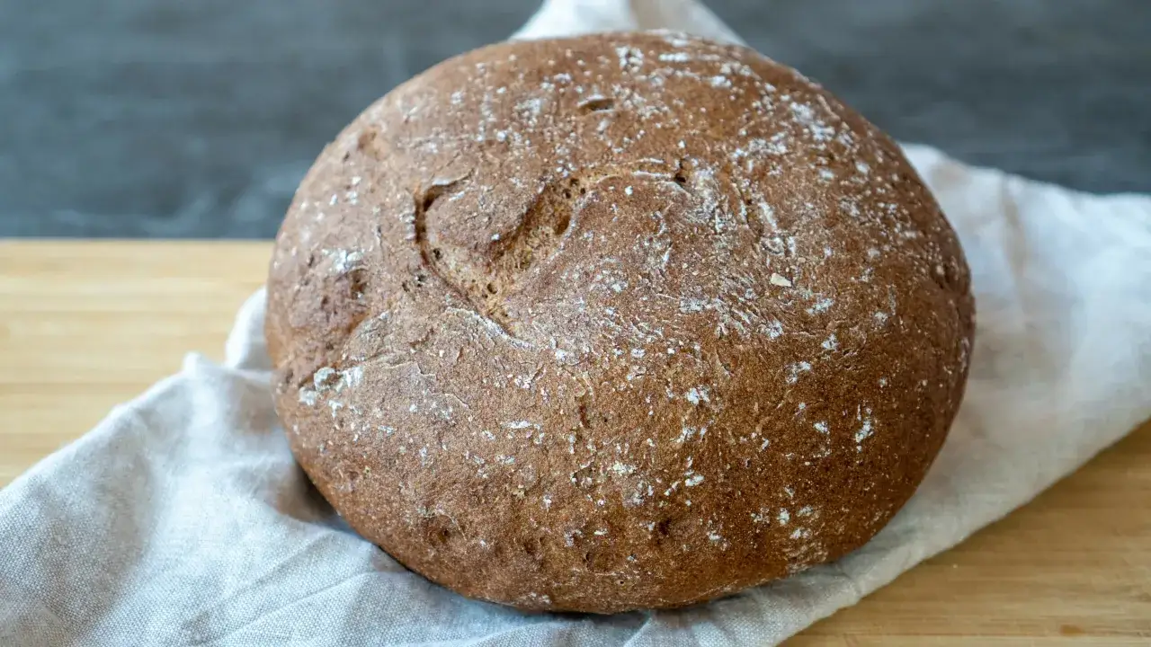 Ein rustikales Brot ohne Mehl, mit einer herzf&ouml;rmigen Vertiefung auf der Kruste, liegt auf einem Leinentuch.