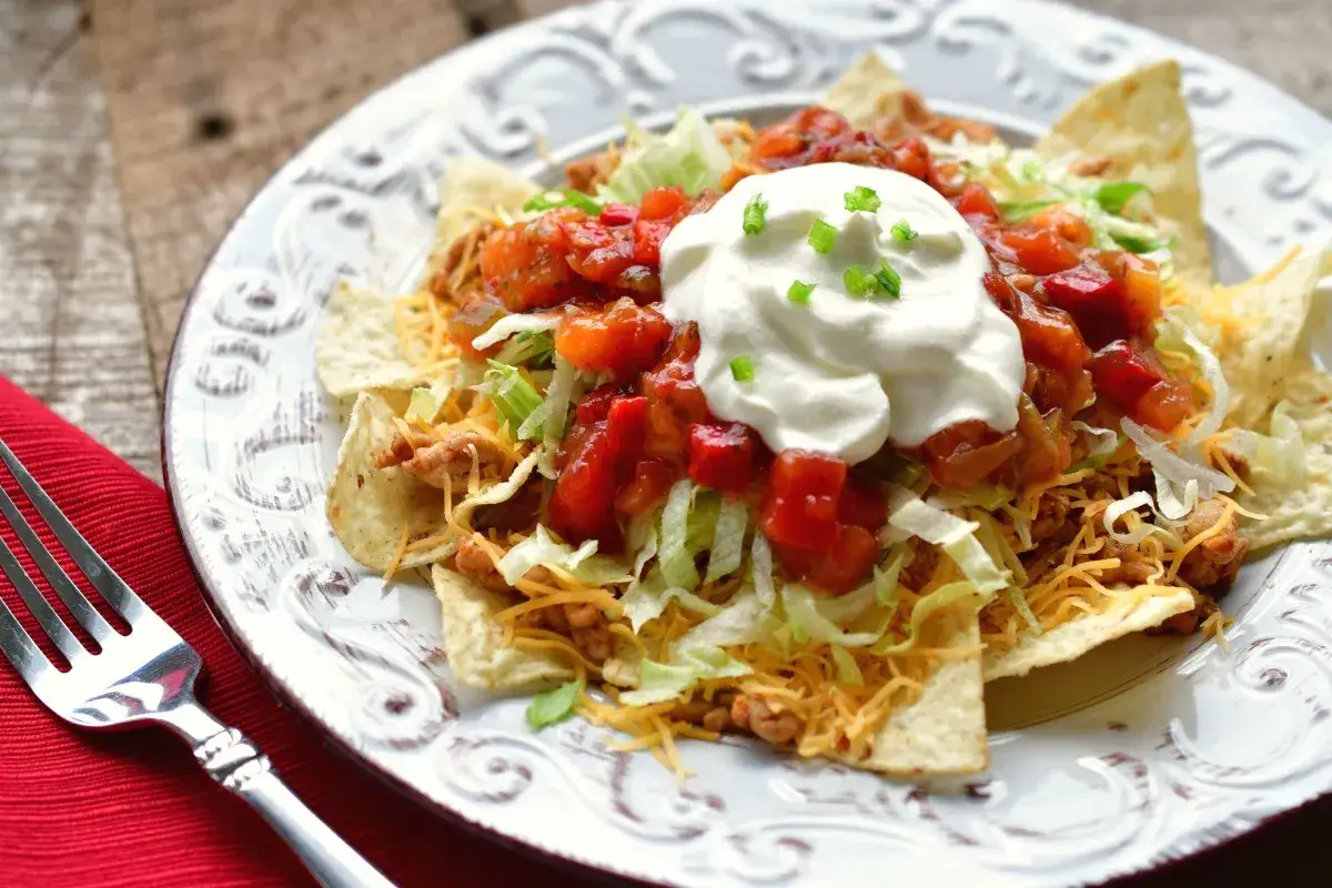 Ein Teller mit einem köstlichen Taco Salat, garniert mit saurer Sahne und Salsa.