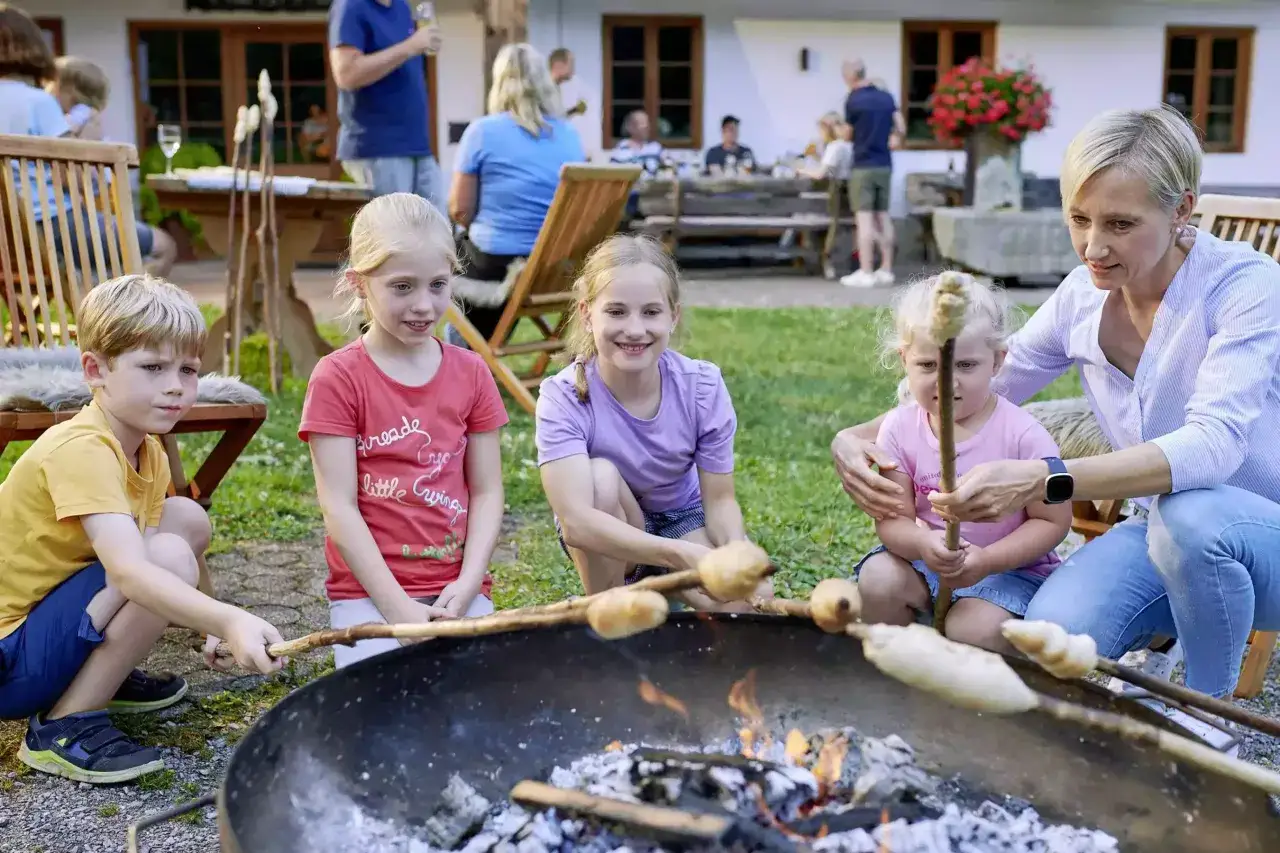 Kinder und eine Frau backen Stockbrot ohne Hefe am Lagerfeuer. Ein fröhlicher Familienmoment im Freien.