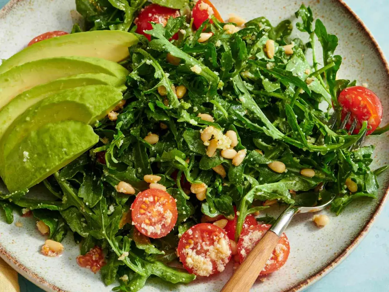 Frischer Rucola Salat mit Kirschtomaten, Pinienkernen und Avocado-Scheiben, appetitlich auf einem Teller angerichtet.