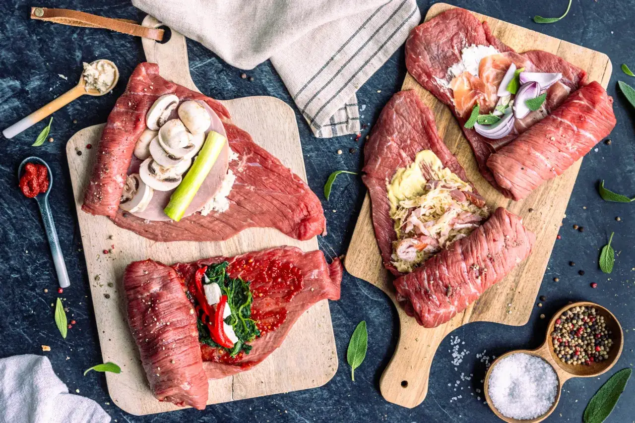 Vorbereitung f&uuml;r ein k&ouml;stliches rouladen rezept: rohes Rindfleisch wird mit verschiedenen Zutaten wie Pilzen, Speck, Zwiebeln und Spinat belegt und auf Holzbrettern angerichtet.