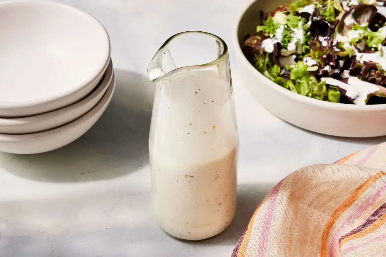 Ein Glas mit cremiger Ranch-Dressing steht neben einer Sch&uuml;ssel Salat.