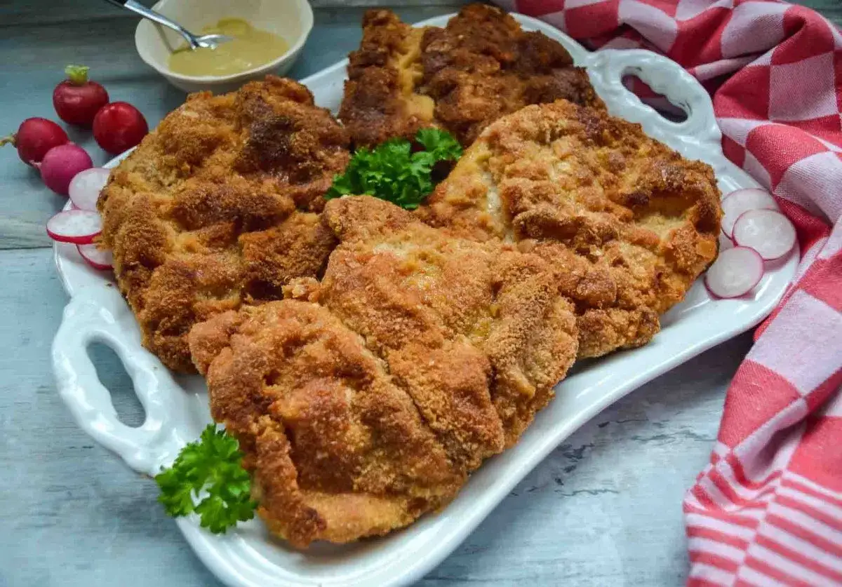 Goldbraune Schnitzel auf einer Platte, perfekt paniert. Ein kleiner Tipp, wie paniert man Schnitzel, um dieses Ergebnis zu erzielen. Dazu Radieschen und Senf.
