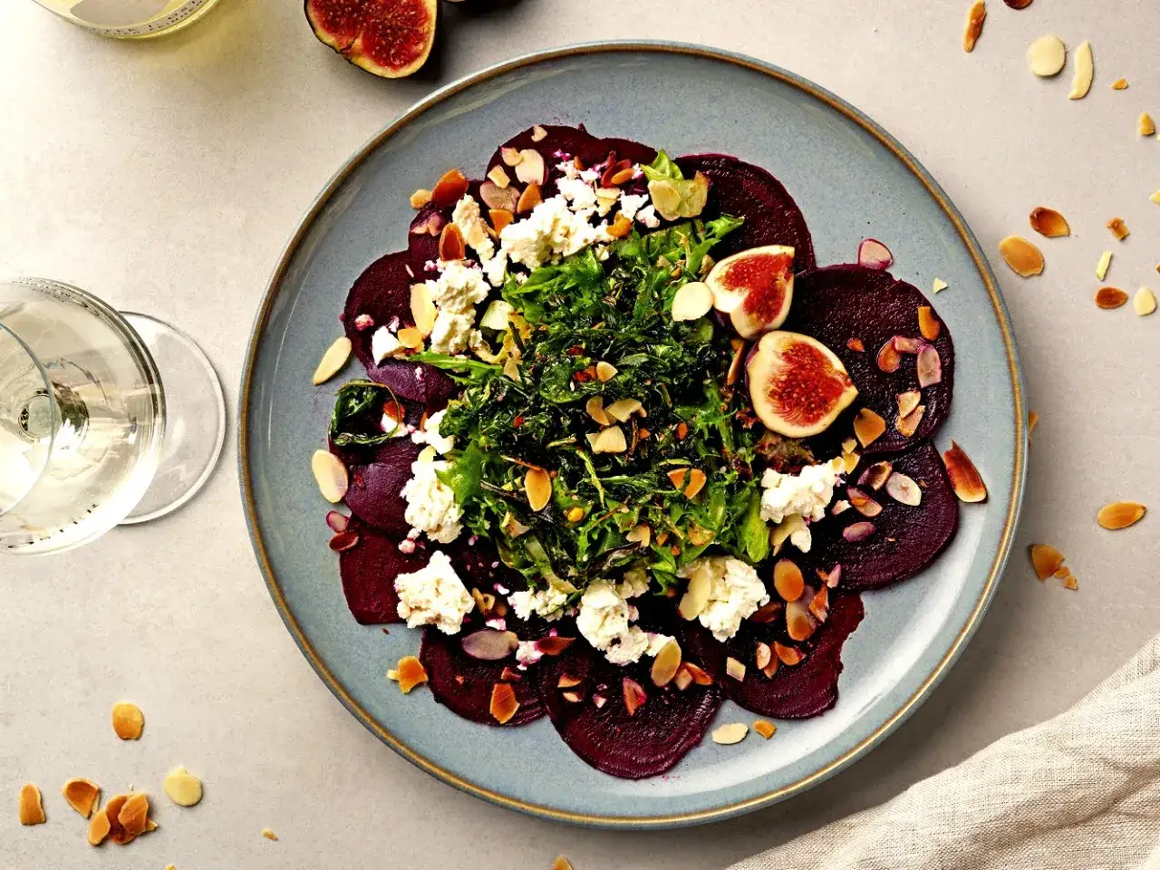 Rote Bete Carpaccio mit Ziegenk&auml;se, Feigen und Mandelsplittern auf einem blauen Teller.