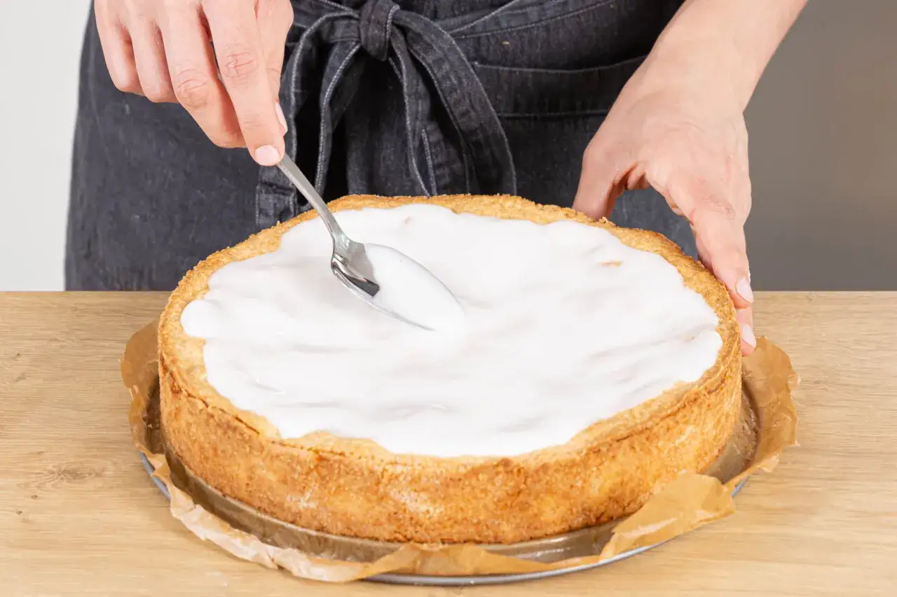 Landfrauen-Apfelkuchen wird mit Zuckerguss verziert. Ein Löffel verteilt die süße Glasur auf dem goldbraunen Kuchen.