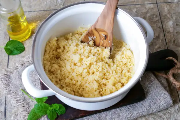 Frisch zubereiteter Couscous in einem Topf, bereit zum Servieren. Ein Holzlöffel lockert die Körner auf.