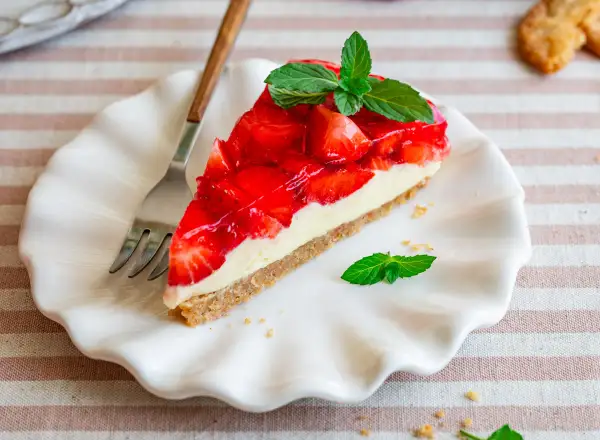 Ein Stück Kuchen ohne Backen mit Keksboden, belegt mit frischen Erdbeeren und Sahne, garniert mit Minze.