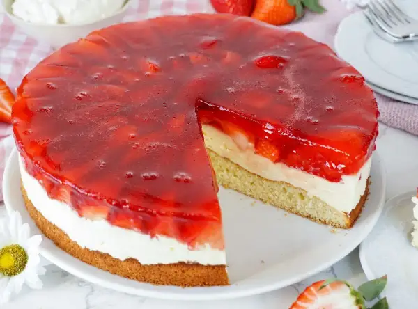 Erdbeerkuchen mit Biskuitboden, Vanillepudding und frischen Erdbeeren unter rotem Tortenguss. Ein saftiges Stück wartet!